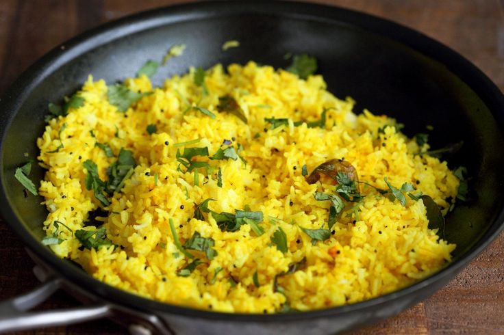 एक कटोरे में ताज़ा हरे धनिये और भुनी हुई मुगफली से सजाया गए सुनहरे lemon rice का एक जीवंत क्लोज अप | 